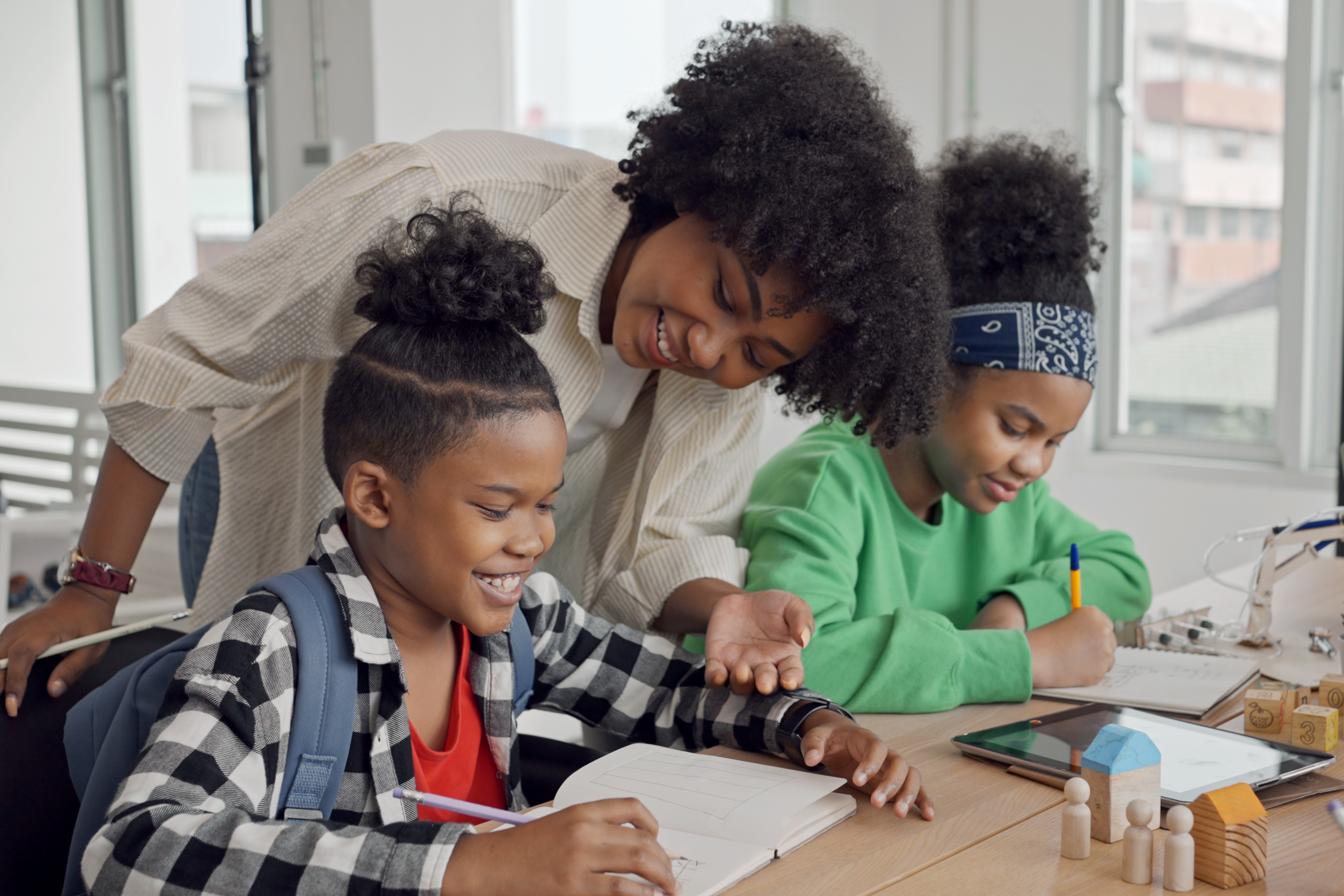 African American female teacher standing with pupils teaching writing lesson in modern classroom.